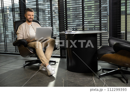 Young bearded man in casual clothes working on laptop Young bearded man in casual clothes working on laptop 112299393
