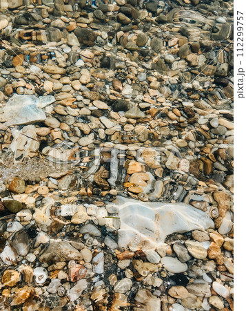Close up sea waves stones shells beach summer day. top view above transparent water. Close up sea waves stones shells beach summer day. top view above transparent water. 112299757