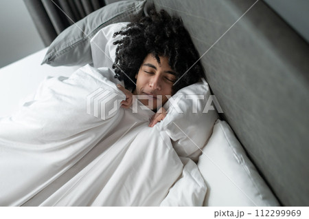 Young brunette man lying in bed and looking sleepy Young brunette man lying in bed and looking sleepy 112299969
