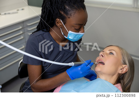 Woman patient sitting in dental chair at medical center while professional doctor fixing her teeth Woman patient sitting in dental chair at medical center while professional doctor fixing her teeth 112300898