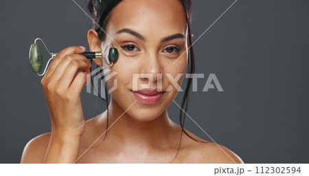 Woman, smile and facial roller for skincare or massage in studio by gray background. Happy model, cosmetics and dermatology for wellness, glow and tool for treatment on skin, beauty and health 112302594