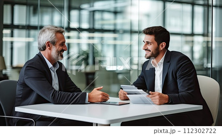 Two business people talking and smiling while sitting at the table in office 112302722