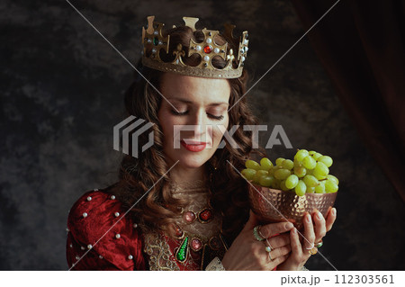 medieval queen in red dress with plate of grapes and crown 112303561
