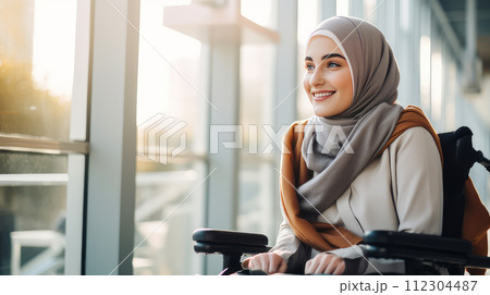 Happy, smiling young Muslim girl student in a wheelchair in the foyer of an educational institution. 112304487