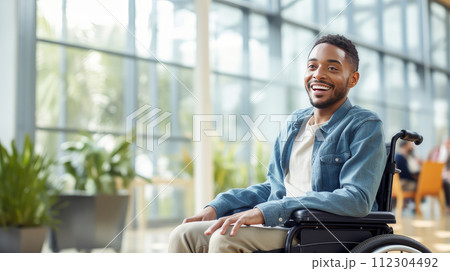 Happy, smiling young dark-skinned, black, African-American guy student in a wheelchair in the foyer of an educational institution. 112304492