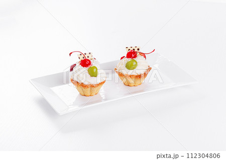 Beautiful cream cakes with cherries and grapes on a plate on a white background 112304806