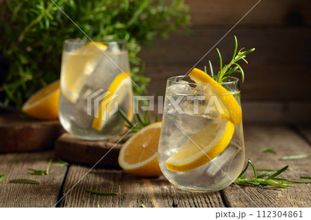 Cocktail gin tonic with ice, lemon, and rosemary on a old wooden table. 112304861