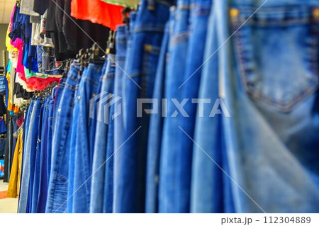 Row of hanged blue jeans in a shop. Clothes store. Shopping in fashion mall. Garments on hangers. Clothes on the store shelves 112304889
