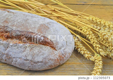 Loaf of bread and ears of grain on wood background. Rustic and rural concept. Close up Loaf of bread and ears of grain on wood background. Rustic and rural concept. Close up 112305073