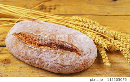 Loaf of bread and ears of grain on wood background. Rustic and rural concept 112305076