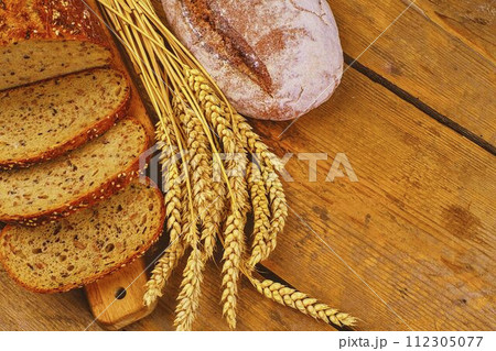Loafs of bread, slices of bread and ears of grain on wood background. Rustic and rural concept. Close up Loafs of bread, slices of bread and ears of grain on wood background. Rustic and rural concept. Close up 112305077