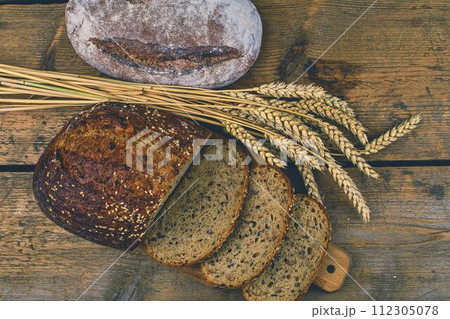 Loafs of bread, slices of bread and ears of grain on wood background. Rustic and rural concept. Close up Loafs of bread, slices of bread and ears of grain on wood background. Rustic and rural concept. Close up 112305078