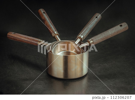 Set of Brass Measuring Cups with Wood Handles with Hanging Hole Design on dark background. 112306207