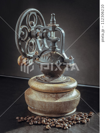 Old original coffee bean original grinder metal shake wheel with hand crank and coffee beans on dark background. Old original coffee bean original grinder metal shake wheel with hand crank and coffee beans on dark background. 112306210