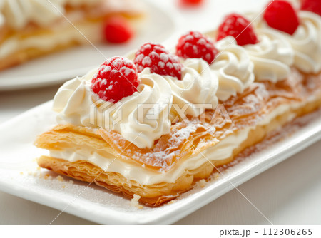 A piece of Napoleon cake or Mille-feuille topped with fluffy whipped cream and vibrant red raspberries 112306265