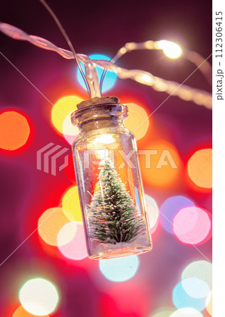 Merry Christmas and happy new year. Hanging small Christmas tree in glass jar on pine branches Christmas tree garland and ornaments over abstract bokeh Merry Christmas and happy new year. Hanging small Christmas tree in glass jar on pine branches Christmas tree garland and ornaments over abstract bokeh 112306415