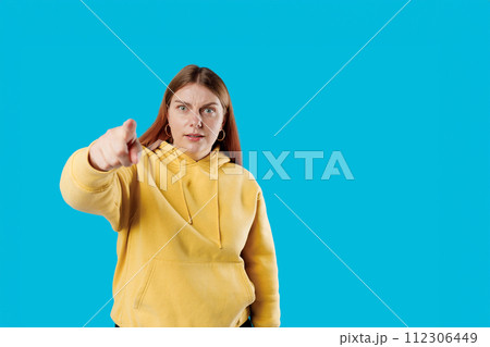 Angry upset woman arguing showing index finger pointing at guilty person punishing mischief in studio, studio portrait. Blue background 112306449