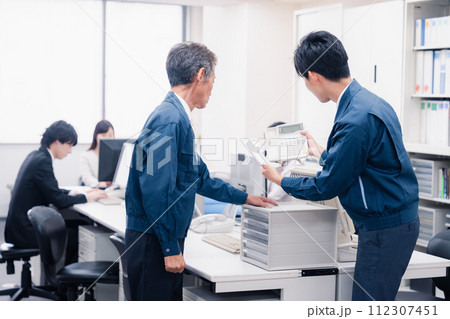 オフィスで電話機のメンテナンスをする作業員の男性 112307451