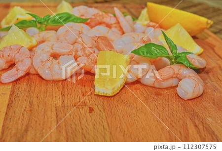 Cooked and peeled prawns with slices of lemon and leaves of basil on chopping board. Food photography. Healthy food. Bio recipe. Copy space 112307575