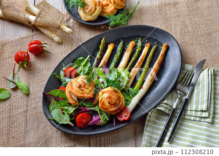 Fried green and white asparagus with mediterranean leaf salads and warm pastry salmon spirals  112308210