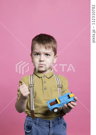 Displeased irritated small boy feeling sad while he plays with a toy car, almost crying in front of the camera. Little child feeling angry and upset holding a plastic blue automobile. Displeased irritated small boy feeling sad while he plays with a toy car, almost crying in front of the camera. Little child feeling angry and upset holding a plastic blue automobile. 112310782