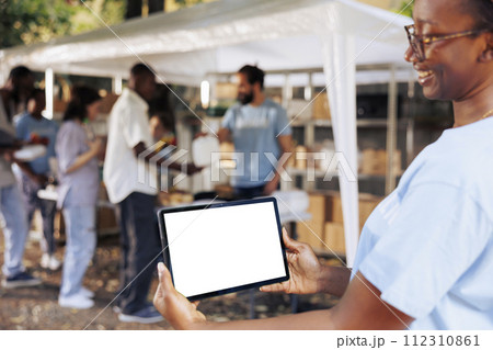 Image shows friendly african american lady carrying tablet with copyspace mockup template for customizable charity notes. Smiling woman horizontally grasps digital device with isolated white screen. 112310861