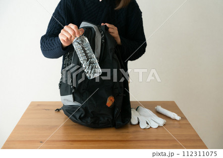 防災リュックにペットボトルを入れる女性 112311075