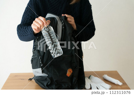 防災リュックにペットボトルを入れる女性 112311076