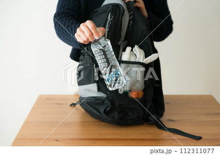 防災リュックにペットボトルを入れる女性 112311077