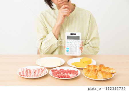 脂質を多く含む食品と電卓を持って悩む女性 112311722
