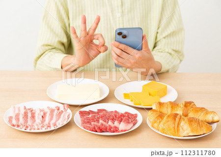 脂質を多く含む食品とスマホを持って丸サインをする女性 112311780
