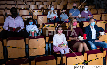Family with child wearing protective masks eating popcorn and watching a movie in cinema Family with child wearing protective masks eating popcorn and watching a movie in cinema 112312486