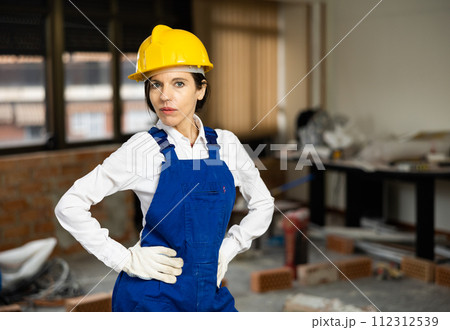 Positive woman repairer in uniform standing inside apartment and looking at camera Positive woman repairer in uniform standing inside apartment and looking at camera 112312539