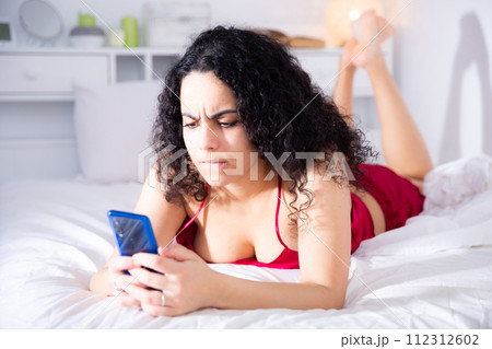 Sexy girl in red lingerie with mobile phone on bed 112312602