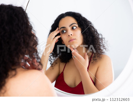 Woman checking her face in mirror in morning 112312603