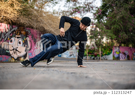 A talented and energetic Asian male hiphop dancer in fashionable clothes is dancing on the street. 112313247