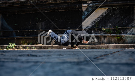 A cool, talented Asian male hiphop dancer is breakdancing on the street in an abandoned street. A cool, talented Asian male hiphop dancer is breakdancing on the street in an abandoned street. 112313307