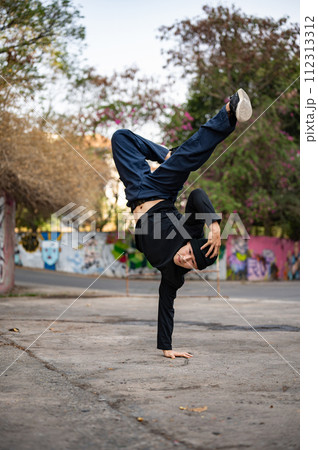 A cool Asian male b-boy dancer or breakdancer is dancing with a one-hand freeze on the street. 112313312