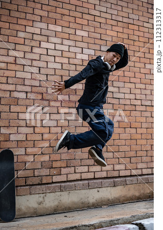 A cool, energetic Asian man is jumping outdoors, practicing his breakdance on the street. 112313317