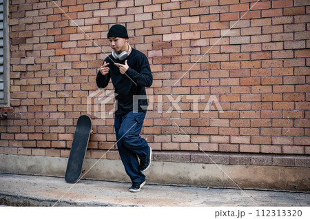 A cool Asian man in fashionable clothes is dancing on the street, practicing his breakdance outdoors 112313320