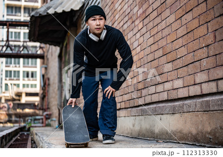 A stylish, hipster Asian male skater is practicing skateboard, skateboarding on the city street. 112313330