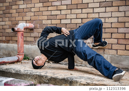 A cool Asian male hip-hop breakdancer is dancing on the street, showcasing his talented movements. 112313396