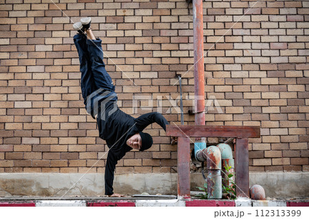 An active Asian male hip-hop breakdancer is dancing on the street in the city, standing on one hand. 112313399