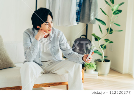 リビングでスマホを見る若い男性 リビングでスマホを見る若い男性 112320277
