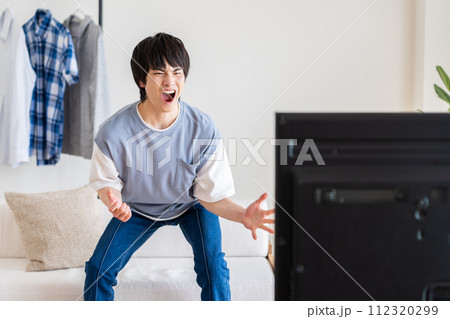 リビングでテレビを見る若い男性 112320299