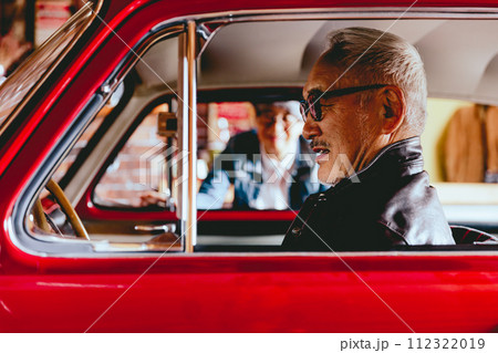 愛車越しに会話をしているシニア夫婦の写真 112322019