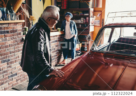 愛車を見ながら会話をしているシニア夫婦の写真 112322024