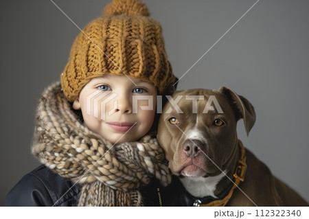 A young boy wearing a brown hat and a scarf is standing next to a brown dog 112322340