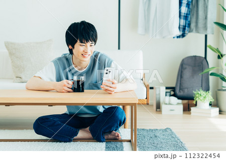 リビングでスマホを見る若い男性 112322454