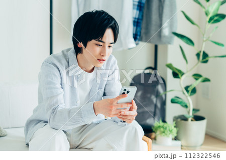 リビングでスマホを見る若い男性 リビングでスマホを見る若い男性 112322546